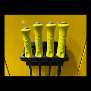 Peut inclure: Quatre outils à manche jaune dans un support noir sur fond jaune. Les outils ont une forme cylindrique avec un dessus argenté et le mot "Snap-on" imprimé sur le côté.