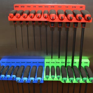 Könnte beinhalten: Ein Satz schwarzer und roter Inbusschlüssel, organisiert auf einem roten und blauen Halter. Die Schlüssel sind mit Größen wie 2 mm, 2,5 mm und 10 mm beschriftet. Der Halter ist auf einer metallischen Oberfläche montiert.