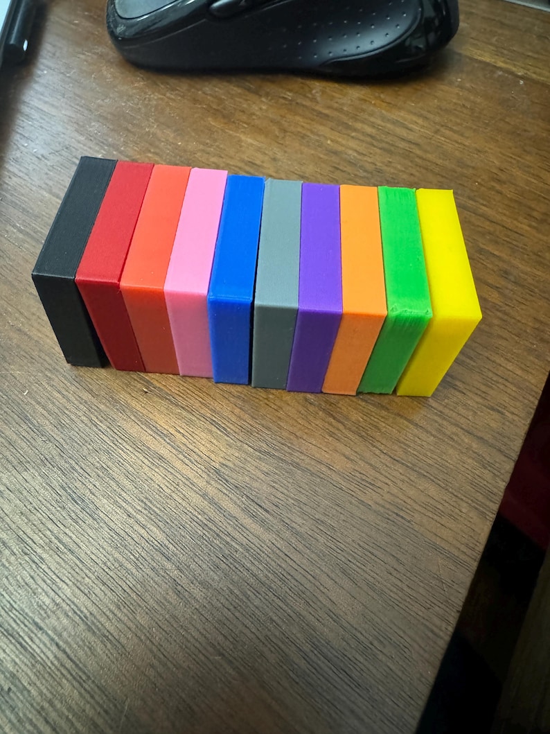 Puede incluir: Una fila de diez bloques rectangulares peque&ntilde;os en varios colores, incluyendo negro, rojo, naranja, rosa, azul, gris, morado, naranja, verde y amarillo.