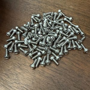 Może przedstawiać: Duża sterta srebrnych śrub na drewnianej powierzchni.