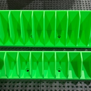 Peut inclure: Deux organisateurs vert vif imprimés en 3D. Chacun comporte plusieurs compartiments verticaux, idéaux pour ranger de petits objets. La conception présente des séparateurs inclinés et de petits trous. Les organisateurs sont rectangulaires.
