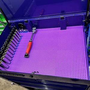 Puede incluir: Un tablero de clavijas morado con una llave roja y negra y un juego de enchufes en una caja de herramientas azul.