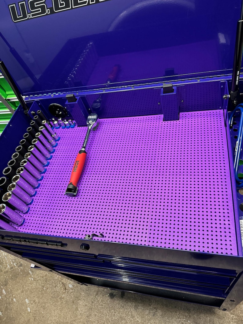 Puede incluir: Un tablero de clavijas morado con una llave roja y negra y un juego de enchufes en una caja de herramientas azul.