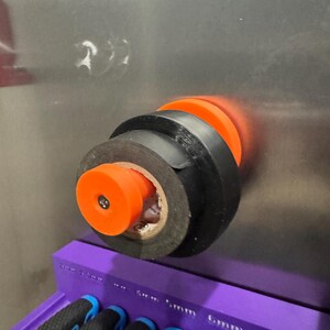 May include: An orange and black tool holder with black electrical tape wrapped around it. The tool holder is mounted on a metallic surface. A purple tool organizer with several tools is visible in the foreground.