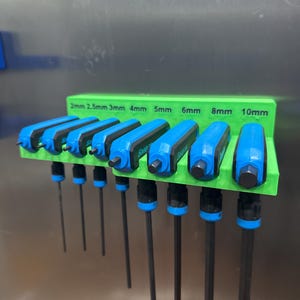 以下が含まれることがあります： 緑色のホルダーに入った六角レンチのセット。レンチは青いハンドルと黒いシャフトが付いています。ホルダーには2mmから10mmまでのサイズが記載されています。工具は整然と配置されており、すぐに使用できます。