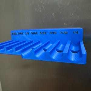 Könnte beinhalten: Ein leuchtend blauer Werkzeughalter mit mehreren Schlitzen und Zoll-Maßen, darunter 3/32, 7/64, 1/8, 9/64, 5/32, 3/16, 7/32 und 1/4. Zur Werkzeugorganisation.