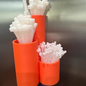 May include: Three orange cylindrical containers holding bundles of white cable ties. The containers are of varying heights and diameters. The background is a brushed metal surface.