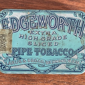 May include: A vintage Edgeworth pipe tobacco tin. The rectangular tin is light blue with dark blue lettering and decorative elements. Text includes "Edgeworth Extra High Grade Sliced Pipe Tobacco" and "Larus & Bro. Co. Richmond, VA, U.S.A."
