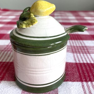 May include: White ceramic sugar or creamer dispenser with a green and white striped design. The lid is shaped like a lemon with a green leaf.