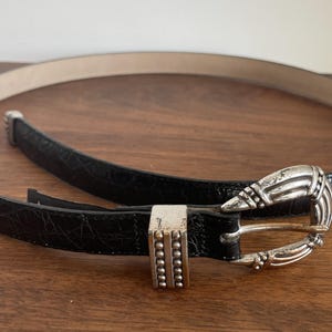 Pu&ograve; includere: Una tazza di ceramica bianca con manico nero e la scritta "But First, Coffee" in nero, con un carattere a mano. La tazza &egrave; su una superficie bianca.