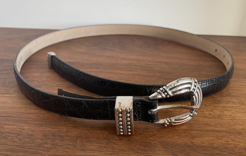 Pu&ograve; includere: Una tazza di ceramica bianca con manico nero e la scritta "But First, Coffee" in nero, con un carattere a mano. La tazza &egrave; su una superficie bianca.