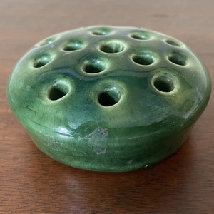 May include: A green ceramic flower frog with multiple holes for arranging flowers.