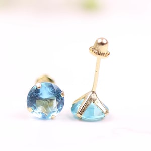 May include: A pair of gold stud earrings with a light blue gemstone. The earrings are on a white surface.