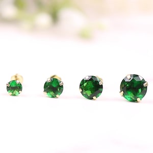 May include: A set of six pairs of gold stud earrings with green gemstones. The earrings are arranged in order of size, with the smallest on the left and the largest on the right.