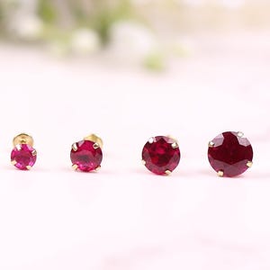 May include: A set of six ruby earrings in different sizes, all with gold settings. The earrings are arranged in a row on a white surface.