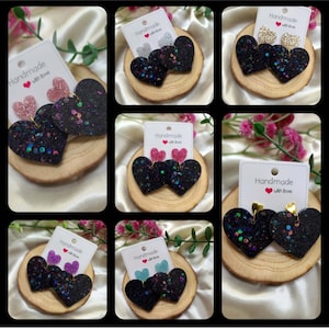 May include: Assortment of handmade heart-shaped earrings with black glitter and various colored glitter accents. Each pair is displayed on a wooden base with a small card that reads "Handmade with love".