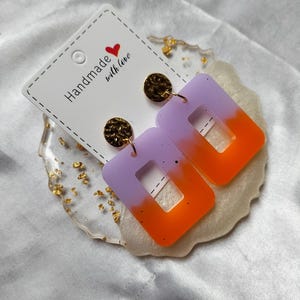 May include: Rectangular handmade earrings with a purple to orange gradient. The earrings are attached to gold-coloured, textured studs. A card with the text "Handmade with love" is also visible.