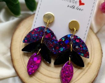 May include: A pair of dangle earrings with a black and pink glitter design. The earrings are handmade with love and feature a gold-tone hook.