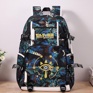 May include: A black backpack with a blue and green pattern, white accents, and black buckles. The front features Japanese text and a gold eye symbol. The backpack has adjustable straps and a top handle.