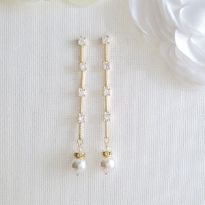 May include: A pair of gold dangle earrings with a pearl drop and a line of clear cubic zirconia stones.