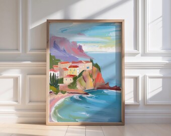 May include: A framed landscape painting depicts a coastal scene with buildings, cliffs, and a beach. The artwork features a palette of blues, pinks, yellows, and greens, with a wooden frame. The painting is displayed against a white wall and wooden floor.