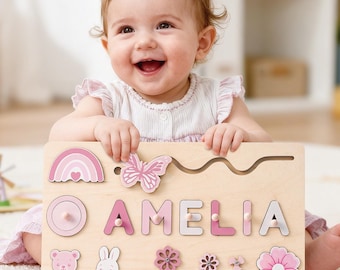 May include: Wooden name puzzle with the name "AMELIA" in pink and white letters. The puzzle includes pink shapes like a rainbow, butterfly, flowers, and a bear and bunny. The puzzle is on a light wood base.