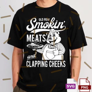 May include: Black t-shirt with a white graphic featuring a pig chef holding a plate of food and giving a thumbs up. The text reads "Old Row Smokin' Meats and Clapping Cheeks."