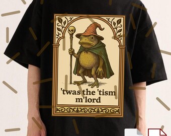 May include: Black t-shirt featuring a whimsical illustration of a frog dressed as a wizard, wearing a hat and cape, holding a staff with a skull. The text reads, "'twas the 'tism m'lord".