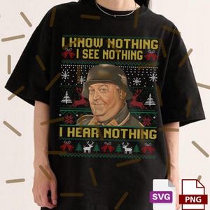 May include: Black t-shirt with a festive design. The shirt features a portrait of a man in a military helmet, surrounded by a pattern of snowflakes, Christmas trees, and reindeer. Text reads "I KNOW NOTHING, I SEE NOTHING, I HEAR NOTHING."