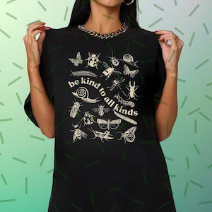 May include: Black t-shirt with a cream insect illustration and the text "be kind to all kinds". The design features various insects, including butterflies, beetles, and snails. The shirt has a crew neck and short sleeves.