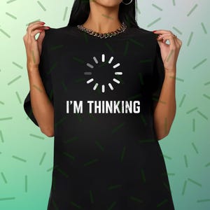 Puede incluir: Camiseta negra con el texto blanco "I'M THINKING" y un símbolo de carga blanco. Esta prenda informal está diseñada para el uso diario. El diseño es sencillo y moderno, adecuado para diversas ocasiones.