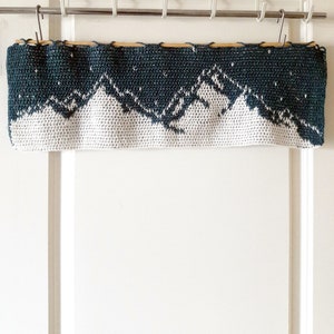 May include: A crocheted wall hanging with a mountain range design in white and teal blue.