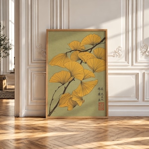 May include: A framed wall art print featuring a botanical illustration of yellow ginkgo biloba leaves on a dark brown branch against a muted olive green background. The artwork includes black calligraphic text and a red square seal in the corner.