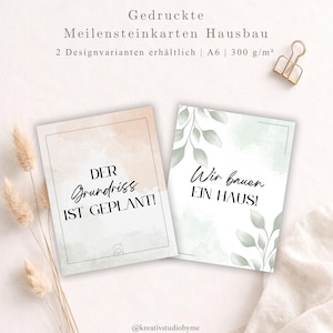 Puede incluir: Dos tarjetas de hitos en alemán con las frases «DER Grundriss IST GEPLANT!» y «Wir bauen EIN HAUS!», con fondos de acuarela y detalles de hojas. Las tarjetas son de tamaño A6 y 300 g/m². Un clip dorado y flores secas también están en la imagen.