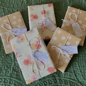 This image shows six of the wrapped up "blind date with a book." Each book is wrapped with brown wrapping paper with white polka dots or floral wrapping paper, white and silver string and has a tag with the genre and a description of the book.