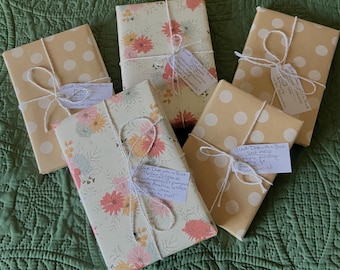 May include: Five wrapped books with different patterned paper. The books are tied with twine and have handwritten notes attached. The notes say "Blind Date with a Book" and include details about the book's genre and author.