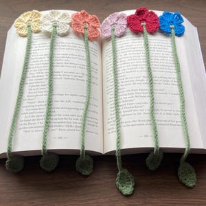 May include: Six crocheted flower bookmarks with green stems and leaves. The flowers are in various colors, including yellow, white, red, pink, and blue.