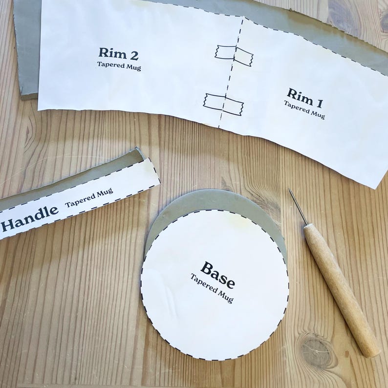 May include: A craft project with paper templates for a tapered mug. The templates include "Rim 2", "Rim 1", "Handle", and "Base". A wooden-handled tool and a gray clay circle are also present on a wooden surface.
