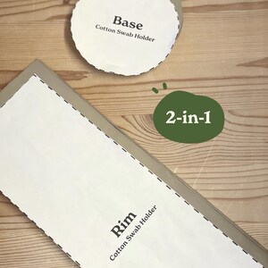 May include: A 2-in-1 cotton swab holder kit with a base and rim. The base is a white circle with the text "Base Cotton Swab Holder". The rim is a white rectangle with the text "Rim Cotton Swab Holder". The kit is on a wooden surface.