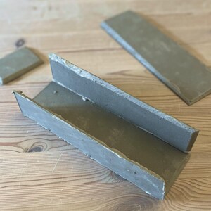 May include: A gray concrete mold for making a rectangular planter. The mold is made of three pieces that fit together to create a trough shape.