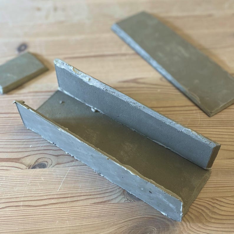 May include: A gray concrete mold for making a rectangular planter. The mold is made of three pieces that fit together to create a trough shape.