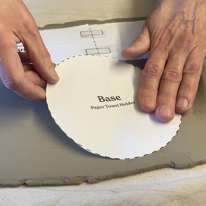 K&ouml;nnte beinhalten: Eine wei&szlig;e Papier-Vorlage f&uuml;r die Basis eines Papierhandtuchhalters. Die Vorlage ist mit "Base Paper Towel Holder" beschriftet und wird auf eine graue Oberfl&auml;che gelegt.