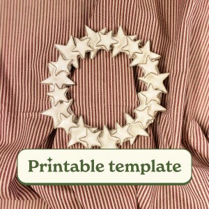 May include: A white star-shaped wreath with a silver outline, resting on a red and white striped fabric. The wreath is made of multiple stars arranged in a circular pattern. The text "Printable template" is displayed on a green rectangular label.
