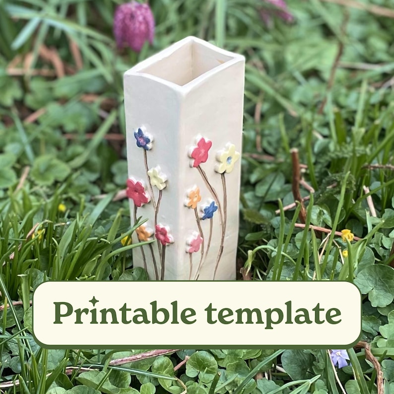May include: A white ceramic vase with a square shape and a rectangular opening at the top. The vase is decorated with colorful flowers in shades of pink, yellow, blue, and green.