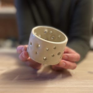 May include: White ceramic candle holder with a circular design and multiple holes.