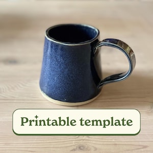 May include: A handmade, navy blue ceramic mug with a speckled glaze. The mug has a wide, slightly flared body and a sturdy handle. The base is unglazed, revealing the natural clay color. The text "Printable template" is displayed on a green banner.