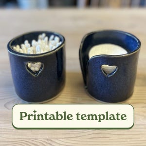 Op de afbeelding: Twee marineblauwe keramische houders met hartvormige uitsparingen. Eén houdt wattenstaafjes vast, de andere wattenschijfjes. De houders hebben een glanzende afwerking en een gouden rand. De tekst "Printable template" staat onderaan.