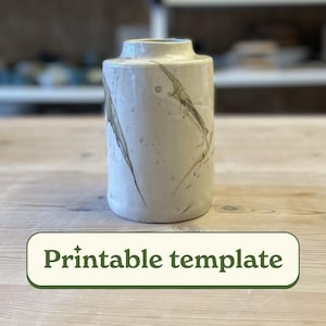 May include: A cylindrical ceramic vase with a speckled, off-white finish and brown marbling. The vase has a slightly flared rim and a label at the bottom that reads "Printable template".