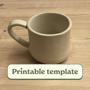 Könnte beinhalten: Eine schlichte, cremefarbene Keramiktasse mit einem abgerundeten Henkel. Die Tasse steht auf einer hellbraunen Holzoberfläche. Der Text "Printable template" ist auf einem grünen Rechteck unter der Tasse gedruckt.