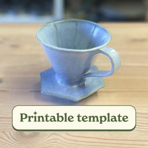 May include: A ceramic pour-over coffee maker in a light blue-gray color. The coffee maker has a handle and sits on a matching hexagonal base. The text "Printable template" is displayed on a green background.